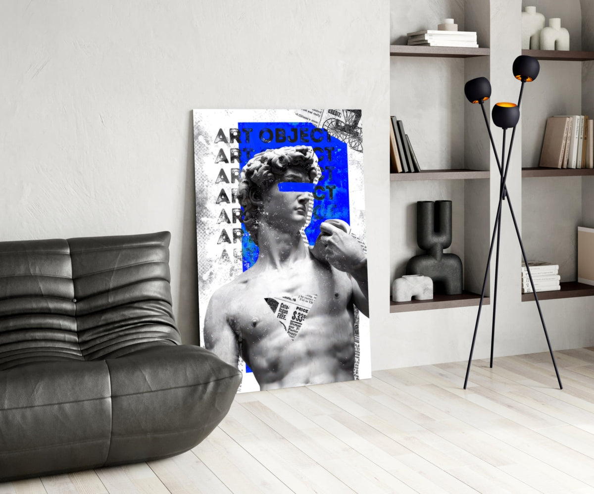 Marble statue on blue newsprint collage glass wall art leaning beside a black leather lounge chair and open shelves