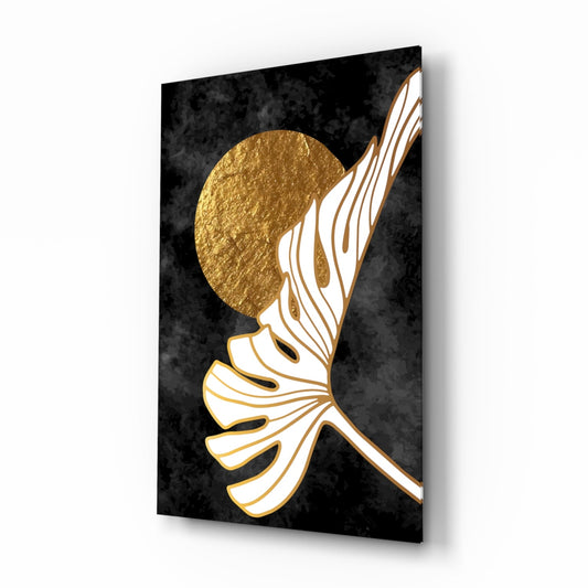 White and gold outlined monstera leaf rising in front of a gold moon on a charcoal background, glass art