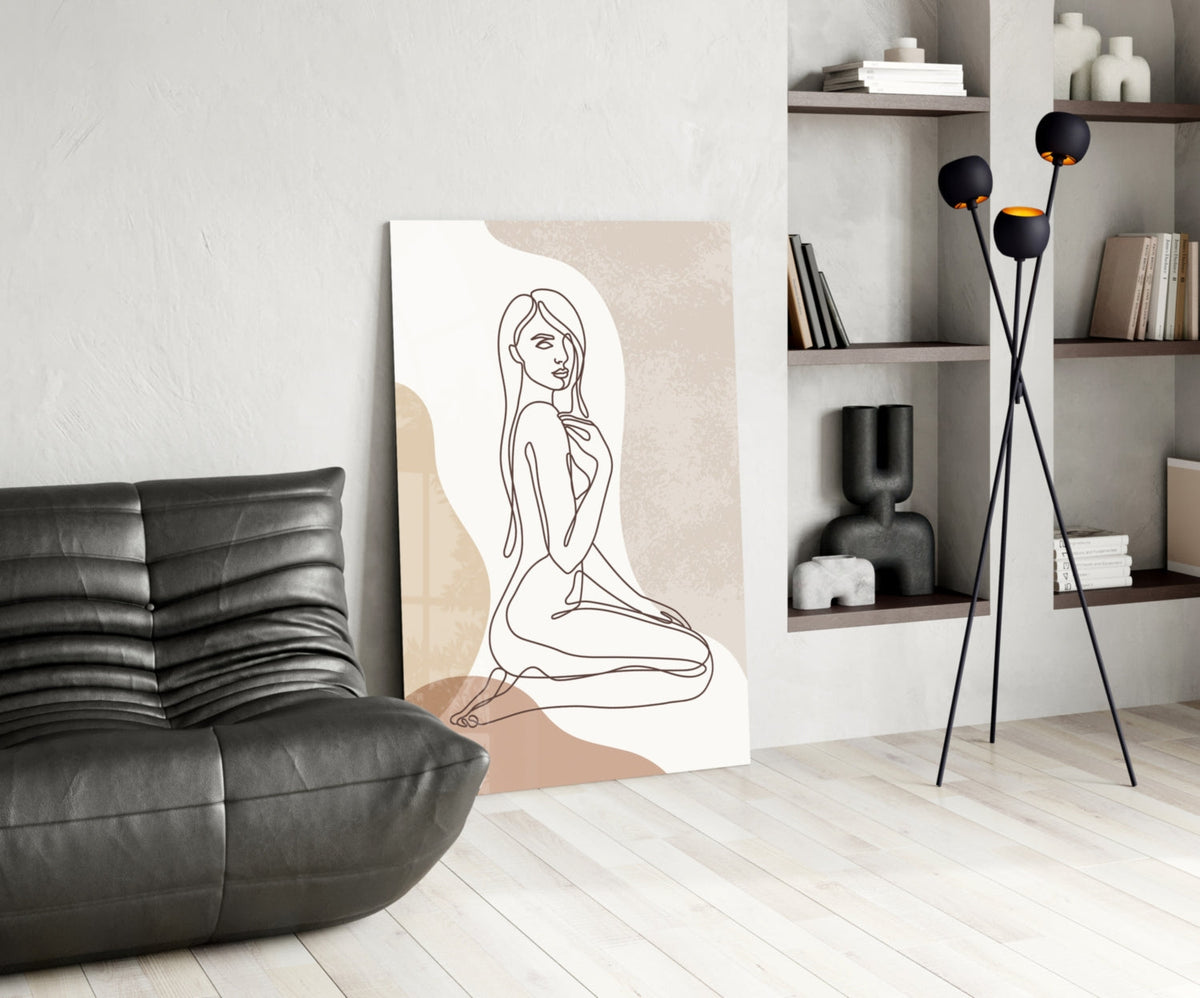 Kneeling woman line art glass print leaning beside a black leather lounge chair and shelves