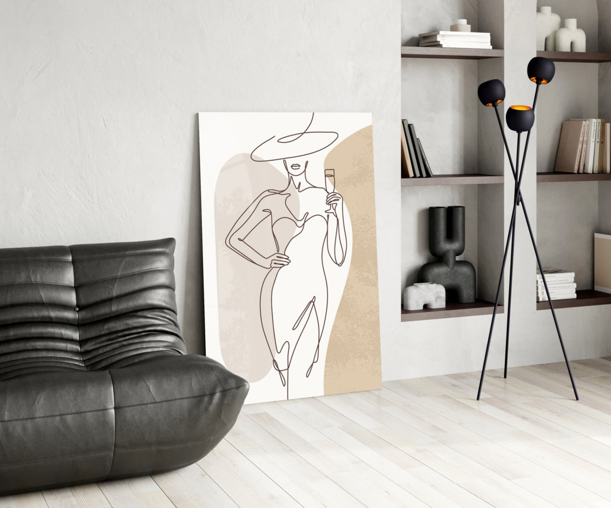 Wide hat line art woman glass wall art leaning on a wall beside a black leather lounge chair and shelves