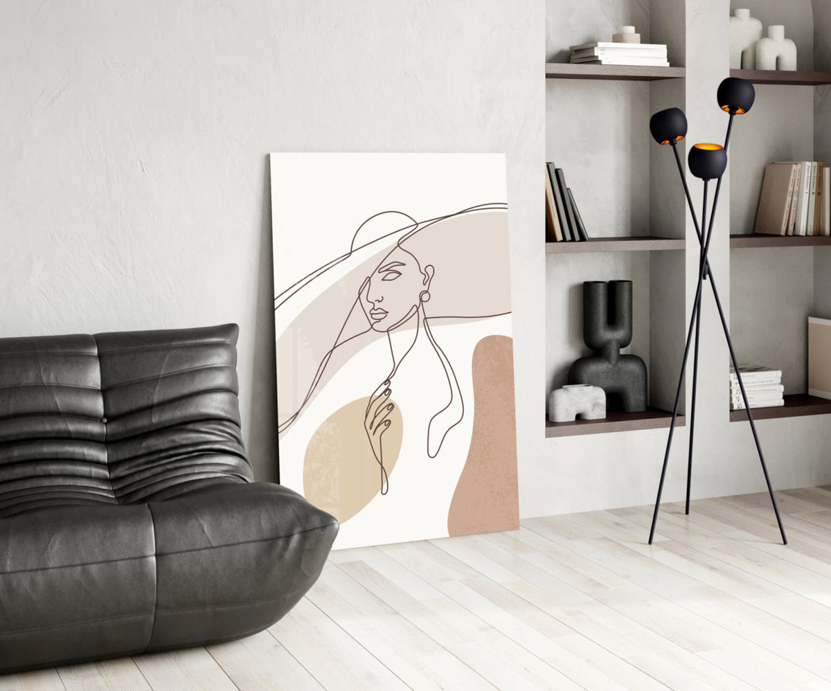Sun hat line art woman glass wall art leaning on a wall beside a black leather lounge chair and shelves