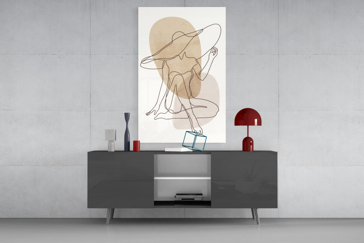 Seated woman line art glass wall art above a dark gray media console with a red lamp