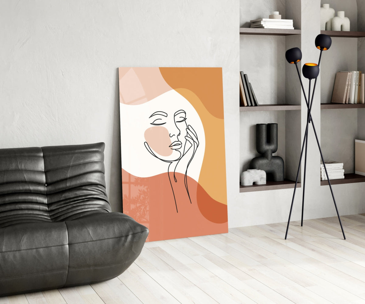 Terracotta line art face glass print leaning beside a black leather lounge chair and shelves