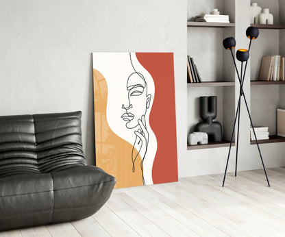 Rust line art face glass print leaning beside a black leather lounge chair and shelves
