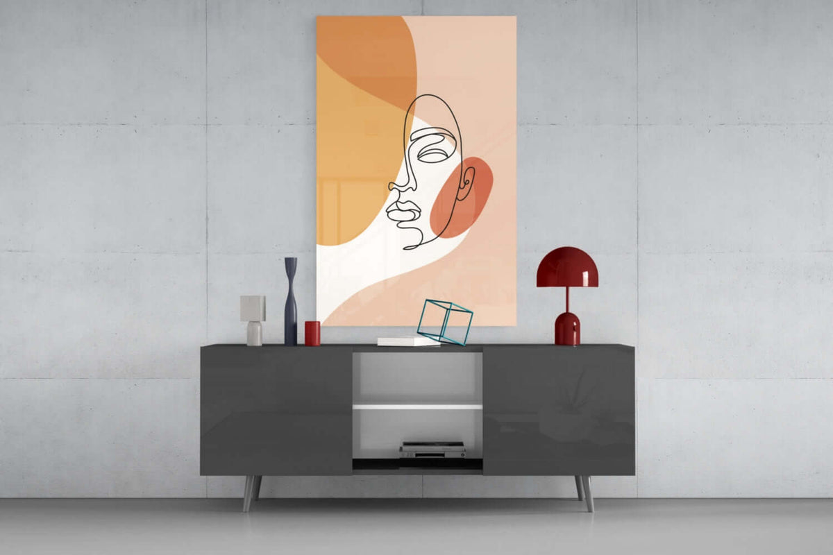 Peach line art face glass wall art above a gray sideboard with a red table lamp