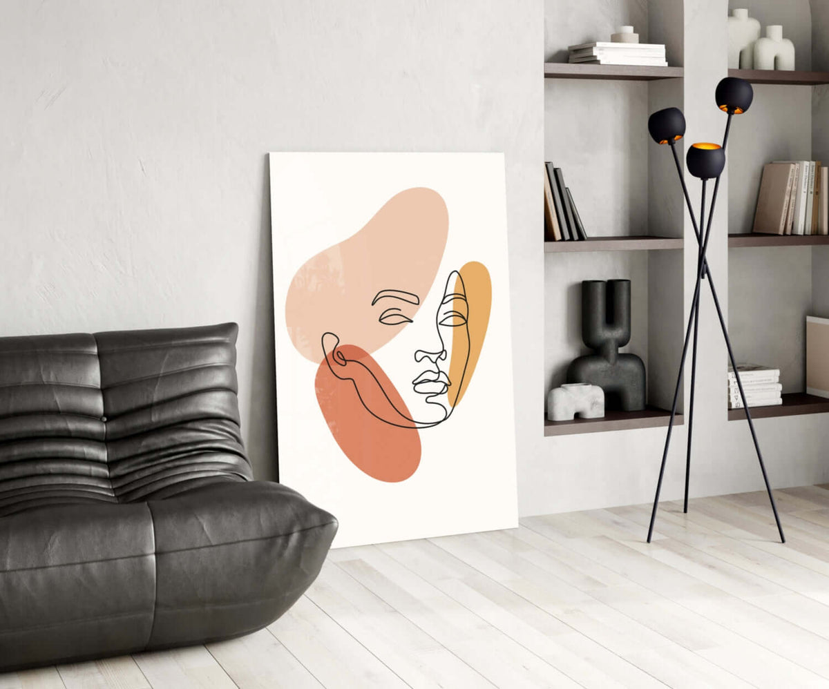 Line art woman face glass wall art leaning beside a black leather lounge chair and open shelves